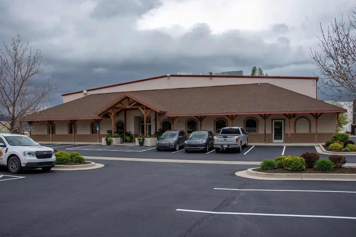 A single-storey office and shop building with a timber-framed covered entry, seen across a parking lot under a stormy sky.